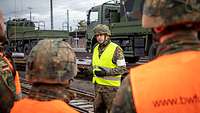 Ein Soldat gestikuliert vor anderen Soldaten im Bahn und Gleisbereich.