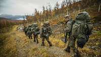 Soldaten marschieren mit Gepäck durch ein bergiges Gelände