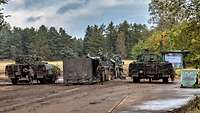 Zwei Panzer stehen auf einer Betonstraße im Gelände neben einem grünen Container.