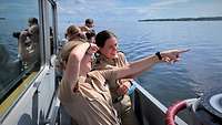 Drei uniformierte Frauen stehen an Bord eines kleinen Schiffes mit Blick auf einen weit entfernten Punkt.