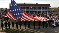 Zahlreiche Soldaten stehen um eine große US-amerikanische Flagge herum.