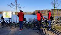 mehrere Personen mit Fahrrädern am Ufer eines Sees