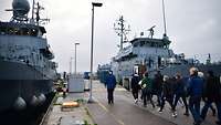 Zwei Boote liegen an der Pier und mehrere Menschen befinden sich auf dem Weg jene zu besichtigen.