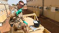Auf einer Zisterne hält ein Soldat mit Handschuhen und Schutzbrille eine lila eingefärbte Probe in den Händen