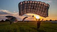 Fallschirmjäger landen auf einer Wiese bei tiefstehender Sonne