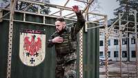 Ein Soldat mit Schutzweste vor einem grünen Container kreist seinen linken Arm 