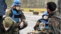 Two blue helmets and two other soldiers are taking care of an injured individual lying on the ground.