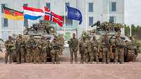 Angetretene Soldaten vor Panzern und die Flaggen von DEU, NLD, NOR, EU wehen am Mast