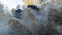 Plenty of muddy water is churned up as an AIFV is crossing a water-filled dip.