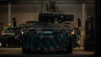 A tank is moving out of a big vehicle hangar.