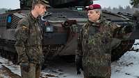 Two soldiers in conversation in front of a tank. 