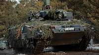 Camouflaged with twigs, a tank is driving along a forest aisle, two soldiers standing in the hatches observing the terrain.