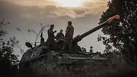 Drei Soldaten stehen auf einer Panzerhaubitze 2000 bei Dämmerung und unterhalten sich