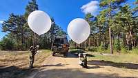 Zwei Soldatinnen präparieren die Ballons vor einem Fahrzeug.