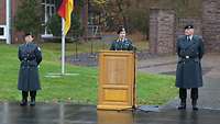 Ein Soldat steht hinter einem Rednerpult und spricht. Links neben dem Pult steht eine Soldatin, rechts ein Soldat.