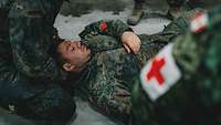 Ein Soldat liegt verwundet am Boden. Er wird von weiteren Soldaten medizinisch versorgt 