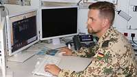 Ein Soldat sitzt an seinem Arbeitsplatz vor mehreren Bildschirmen