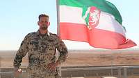 Ein Soldat steht in einem Bundeswehrcamp neben einer gehissten Flagge von Nordrhein-Westfalen