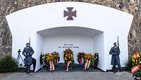 Zwei Soldaten im grauen Mantel stehen neben dem Ehrenmal und präsentieren das Gewehr.