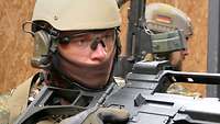 Ein Soldat in Gefechtsausrüstung hält sein Gewehr im Anschlag und beobachtet die Situation.