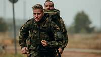 Soldatin mit Rucksack joggt vor einem Soldaten
