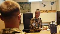 Eine Frau in Uniform sitzt vor einem Computer und berät einen Mann in Uniform