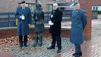 Zwei Soldaten und ein Zivilist stehen links und rechts von einer Bronzestatue.