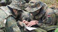 Soldaten liegen auf dem Waldboden, in ihrer Mitte eine Karte, mit deren Hilfe sie ihr Vorgehen planen.