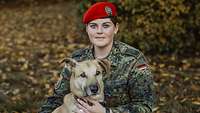Eine Soldatin mit rotem Barett hockt neben einem Hund und umarmt ihn
