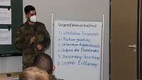 Ein Soldat steht vor einer Flipchart und führt eine Lernzielkontrolle durch.