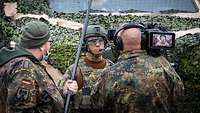 Zwei Soldaten mit Kamera und Mikrofon interviewen einen Soldaten draußen vor einem getarnten Fahrzeug.