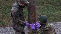 Two soldiers mould plastic explosive around a tree trunk.