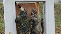 Two soldiers install a wooden door in a solid concrete frame.