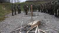 Im Vordergrund liegt ein gesprengter Holzstamm, dahinter stehen Soldaten im Halbkreis, ein Soldat erläutert.