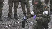 A soldier kneels next to the combat boot damaged in the explosion. He shows where the hole in the boot is.