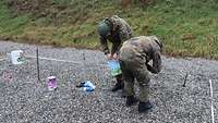 Two solders build a wire frame from which two buckets are suspended.