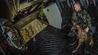 Ein Soldat sitzt neben einem Hund in einem fliegenden Hubschrauber mit geöffneter Heckklappe