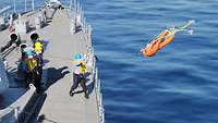 Ein Dummy wird von mehreren Personen von einem Schiff ins Wasser geworfen