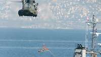 Ein Hubschrauber fliegt dicht über einem Schiff in See