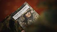 Ein Soldat hält ein Buch mit einem bunten Cover.