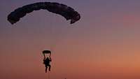 Ein Fallschirmjäger nähert sich im Sonnenuntergang dem Boden.