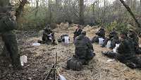 Jugendliche in Uniformen sitzen im Kreis auf hellem Stroh im Wald.