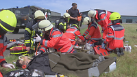 Rettungskräfte knien auf dem Boden und versorgen die Verletzten. Sie legen einen Tropf bei einer der Spezialpuppen. 