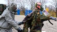 Ein Kamerad wird von einem Dekontaminationssoldaten von seiner dekontaminierten Uniform befreit. 