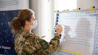 A Hungarian soldier writes with a pen in a list on a whiteboard