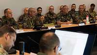 Zahlreiche Militärexperten verschiedener Länder besprechen sich sitzend an Tischen.