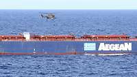 Ein Hubschrauber fliegt über einem zivilen Handelsschiff, während ein Soldat mit einem Seil an Bord des Frachters geht