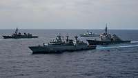 Vier graue Kriegsschiffe fahren nebeneinander parallel in See.