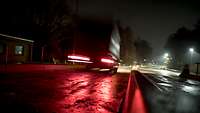 Ein Fahrzeug, unscharf von hinten zu sehen, fährt mit Licht bei Dunkelheit auf einer Straße.