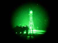 Blick durch ein Nachtsichtgerät vom Typ Bonie-M. In einem grünen Lichtkreis stehen Soldaten neben einem Fahrzeug vor einem Mast.